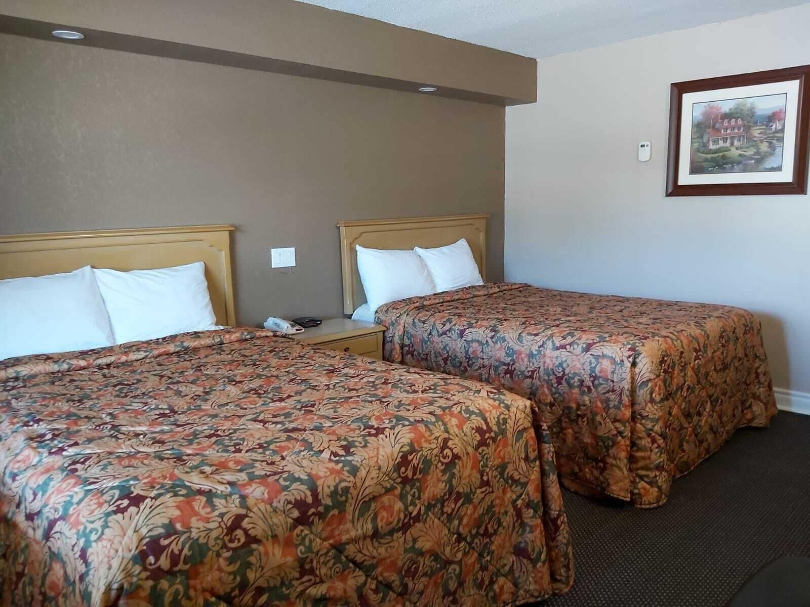 Quarto de hotel com duas camas, cada uma com roupa de cama estampada com motivos florais, mesa de cabeceira com telefone e quadro na parede.