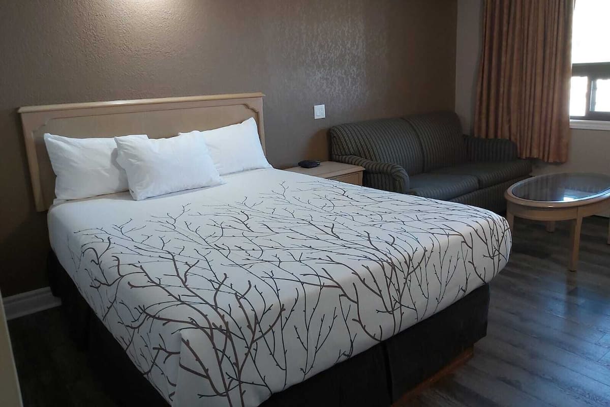 A hotel room with a bed, a sofa, a small table, and a window with curtains.