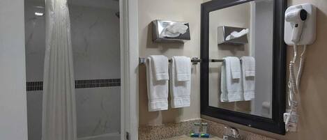 A bathroom with a shower, toilet, sink, and a mirror with a hand dryer.