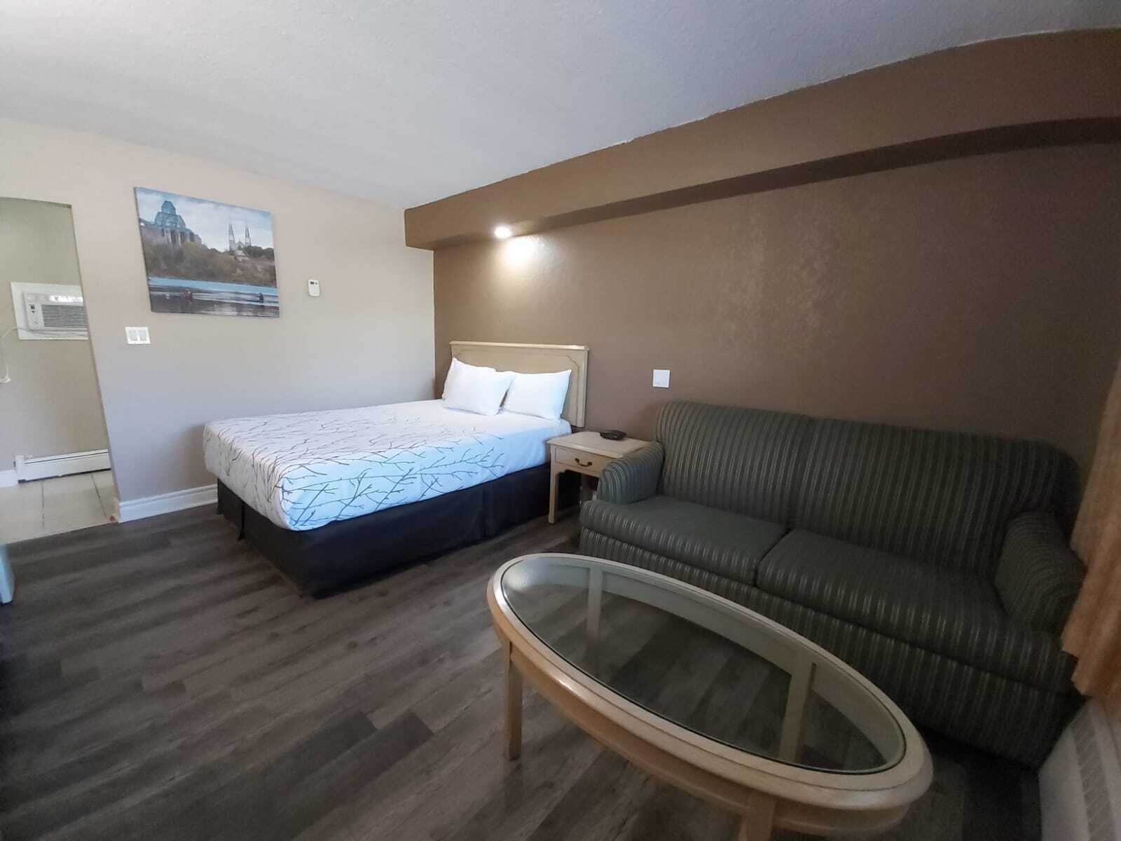 Habitación de hotel con cama, sofá, una mesa con superficie de vidrio y un aire acondicionado instalado en la pared.