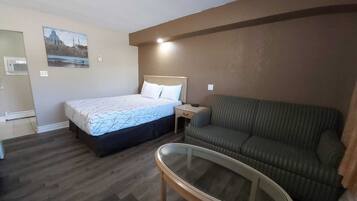 Habitación de hotel con cama, sofá, una mesa con superficie de vidrio y un aire acondicionado instalado en la pared.