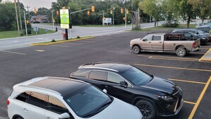 Un parking où sont garées plusieurs voitures, dont un SUV blanc et un SUV noir, ainsi qu’un pick-up.