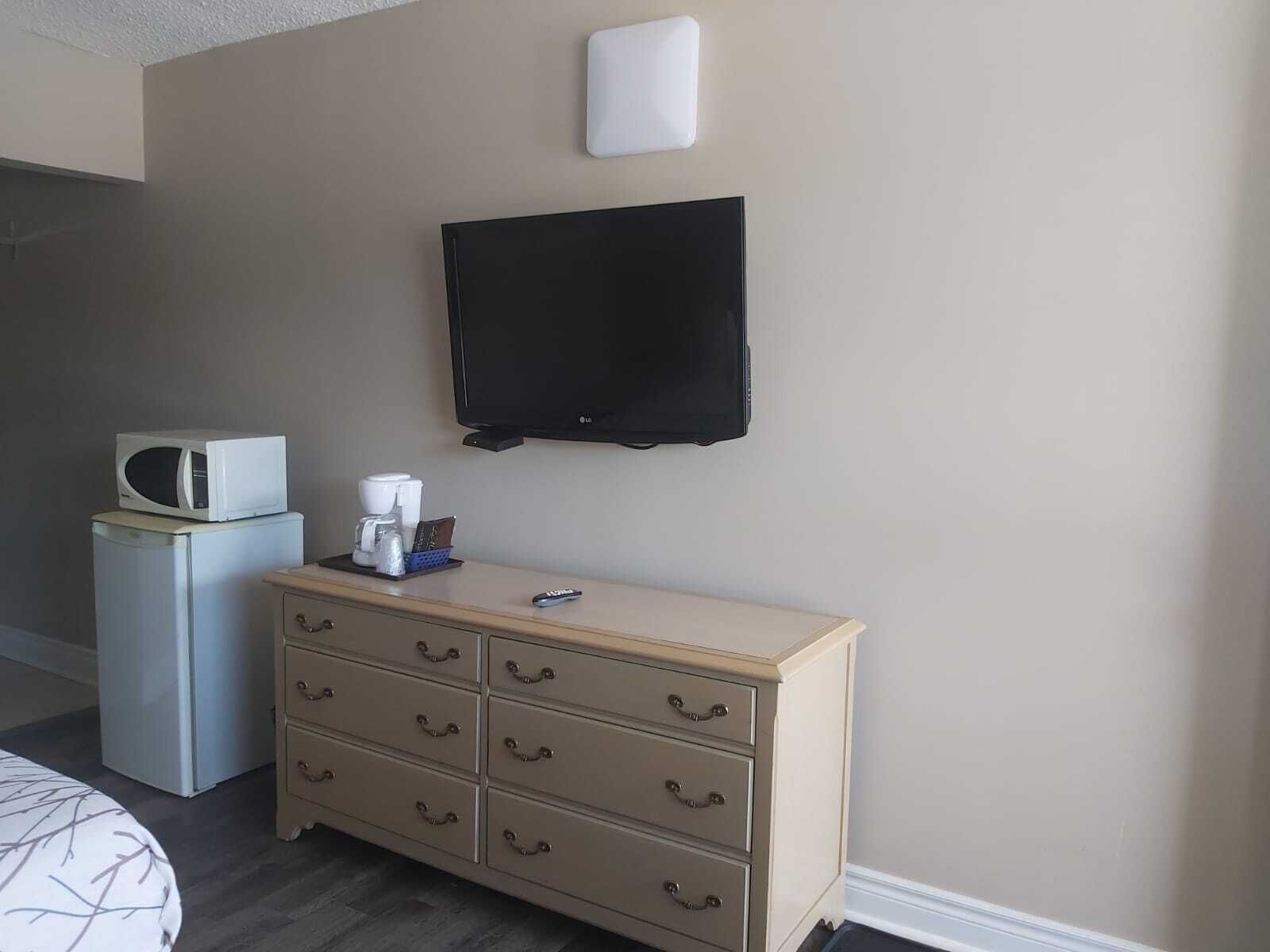 Une chambre d’hôtel équipée d’un lit, d’une commode avec des tiroirs, d’un four à micro-ondes, d’une machine à café et d’un téléviseur à écran plat fixé au mur.