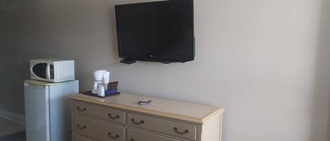 Une chambre d’hôtel équipée d’un lit, d’une commode avec des tiroirs, d’un four à micro-ondes, d’une machine à café et d’un téléviseur à écran plat fixé au mur.