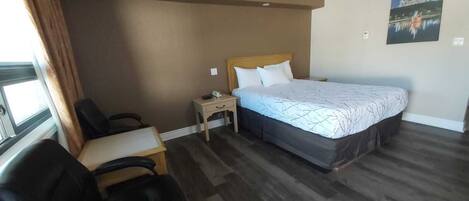 A hotel room with a bed, a desk, a chair, a nightstand, and a window with curtains.