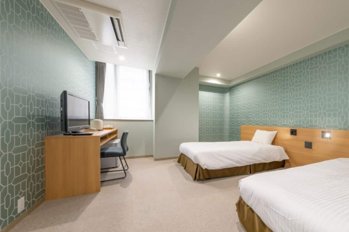 A hotel room with two beds, a desk with a computer, and a window.