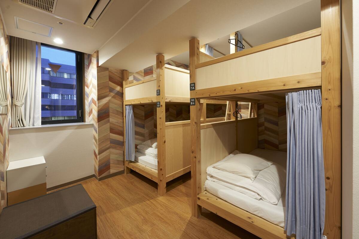 A dormitory room with bunk beds, a desk, and a window with curtains.