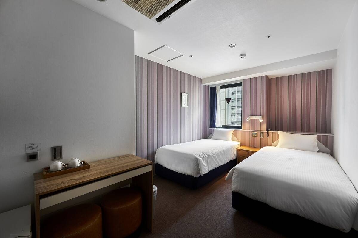 A hotel room with two beds, a desk, a chair, a window, and a nightstand.