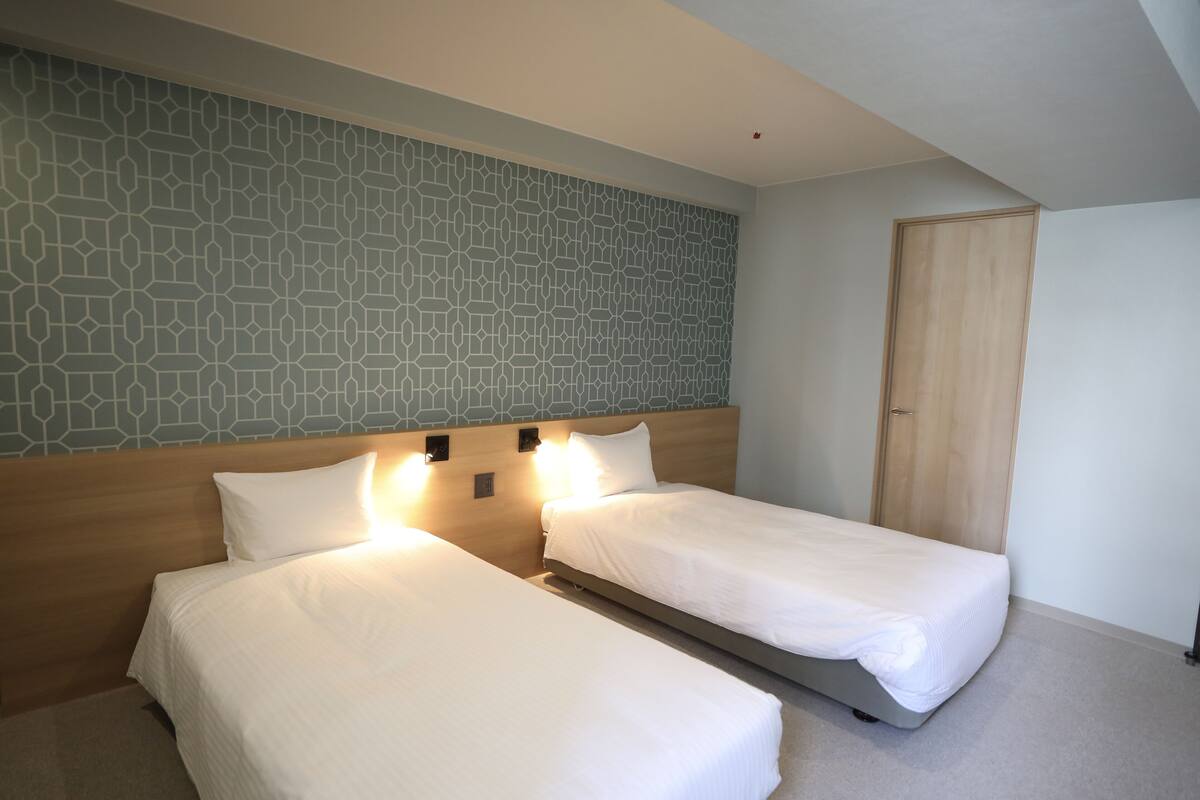 A hotel room with two beds, a patterned wall, and a wooden door.