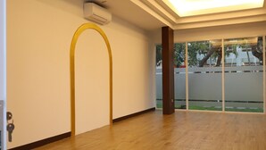 Ruime kamer met houten vloer, een brede gewelfde deuropening en uitzicht door een glazen deur naar buiten.