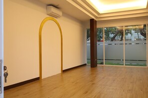 Ruime kamer met houten vloer, een brede gewelfde deuropening en uitzicht door een glazen deur naar buiten.