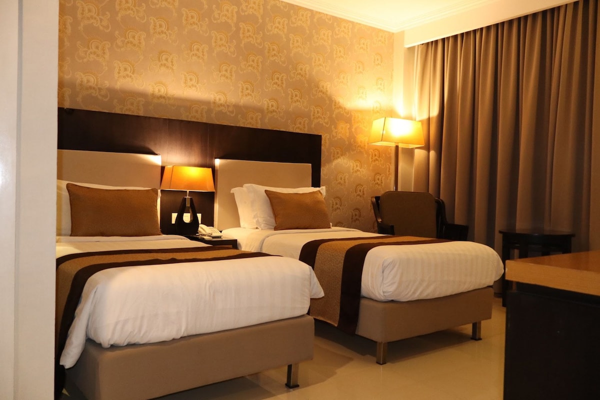 Une chambre d’hôtel avec deux lits, un bureau, une chaise et une lampe.
