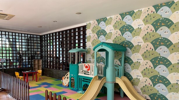 Un espace de jeux pour enfants avec un toboggan, une cabane et un sol coloré.