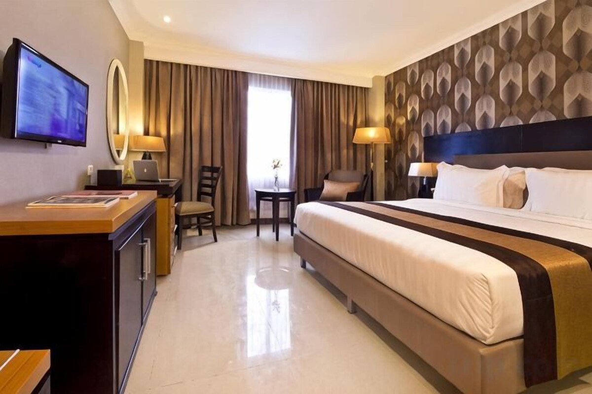 Een hotelkamer met een bed, bureau, stoel, televisie en een groot raam met gordijnen.