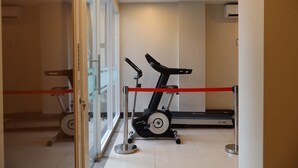 Een sportschool met twee loopbanden en een hometrainer, gescheiden door een rode barrière.