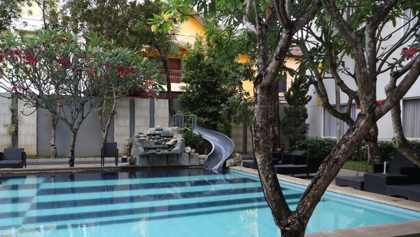 A swimming pool with a slide, surrounded by trees and outdoor seating.