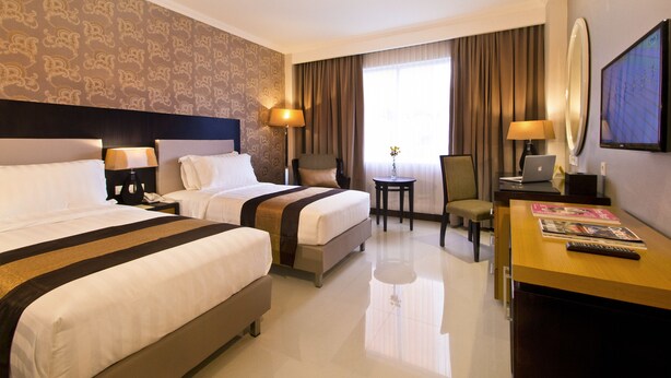 A hotel room with two beds, a desk, a chair, a laptop, and a TV. - Gets Premiere Yogyakarta (Depok)