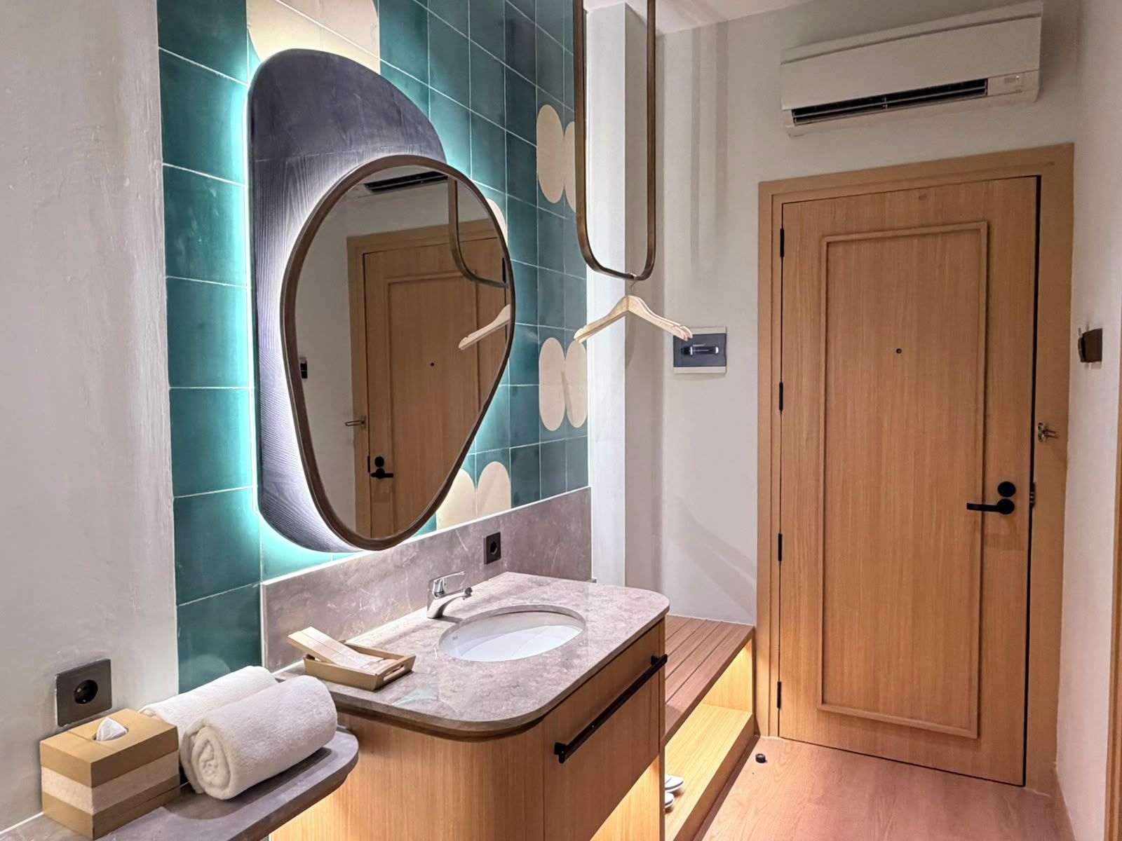 Un baño moderno con un tocador curvo, un espejo grande y una puerta de madera.