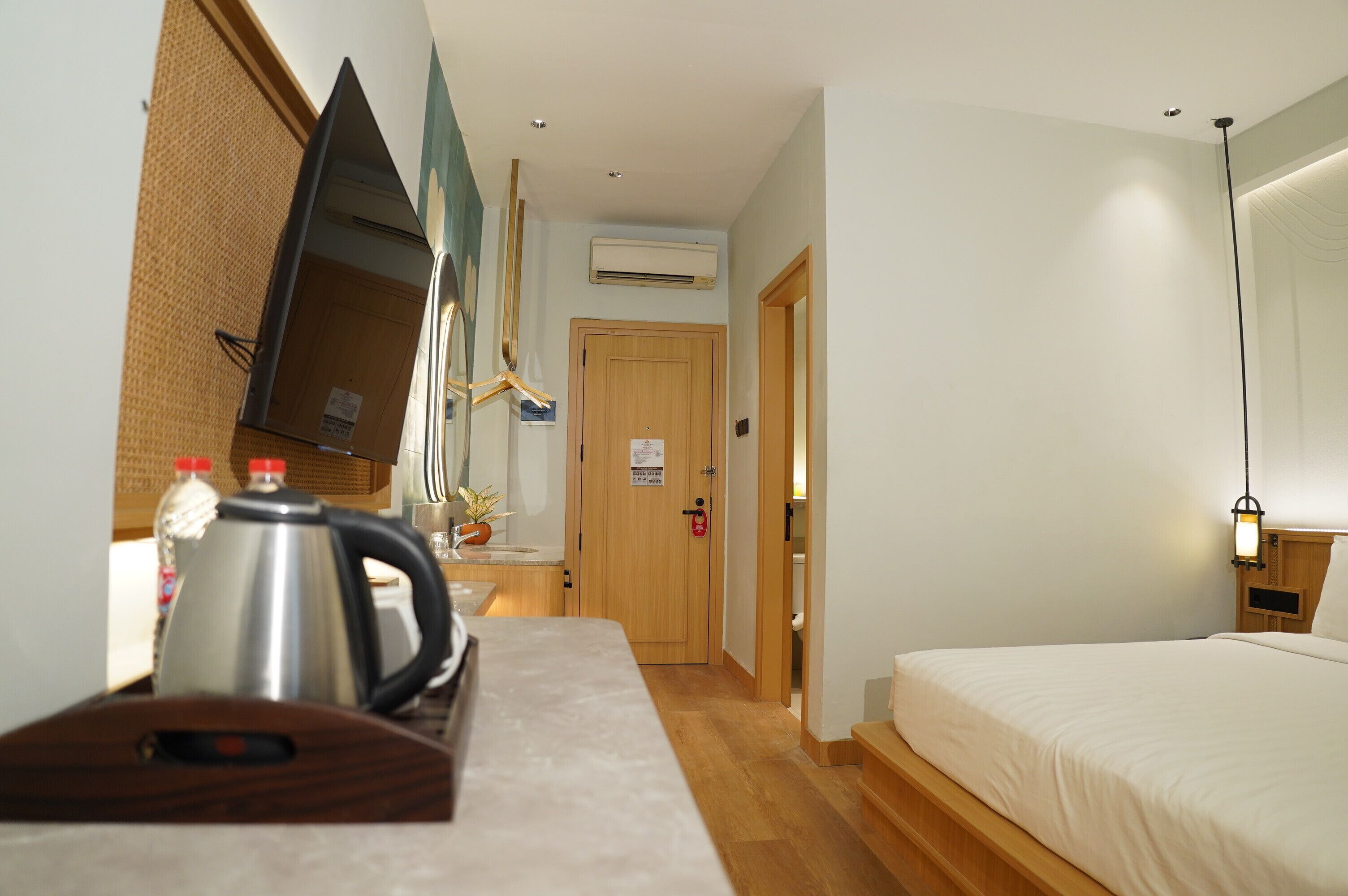 Habitación de hotel con cama, escritorio con tetera, televisor y puerta que da a un baño.