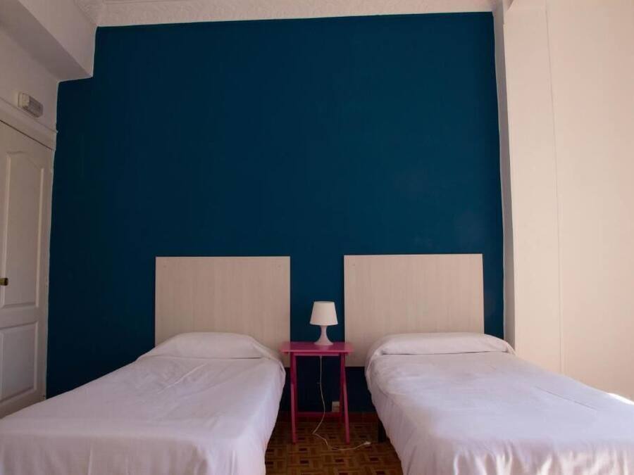 Una habitación con dos camas individuales, una mesita de noche con lámpara y una puerta.