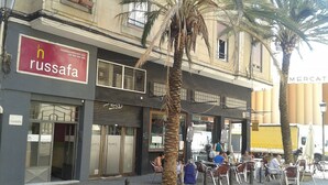 A building with a 'Russafa' sign, outdoor seating, and palm trees. - Russafa Youth Hostel (Valencia)