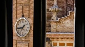 A clock on a brick wall with a view of a building with a fountain. - Russafa Youth Hostel (Valencia)
