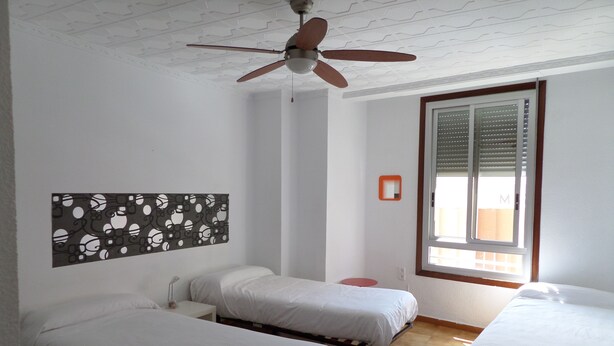 A room with three single beds, a ceiling fan, a window with blinds, and a wall-mounted mirror. - Russafa Youth Hostel (Valencia)