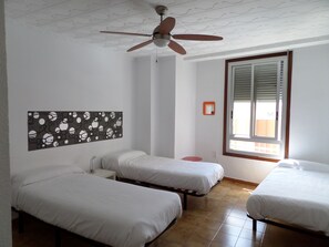 A room with three single beds, a ceiling fan, a window with blinds, and a wall-mounted mirror. - Russafa Youth Hostel (Valencia)