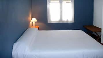Una cama individual con sábana blanca en una habitación con paredes azules y una ventana.