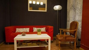 A room with a red sofa, a white coffee table, a wooden chair, a floor lamp, and a wall with a drawing. - Russafa Youth Hostel (Valencia)