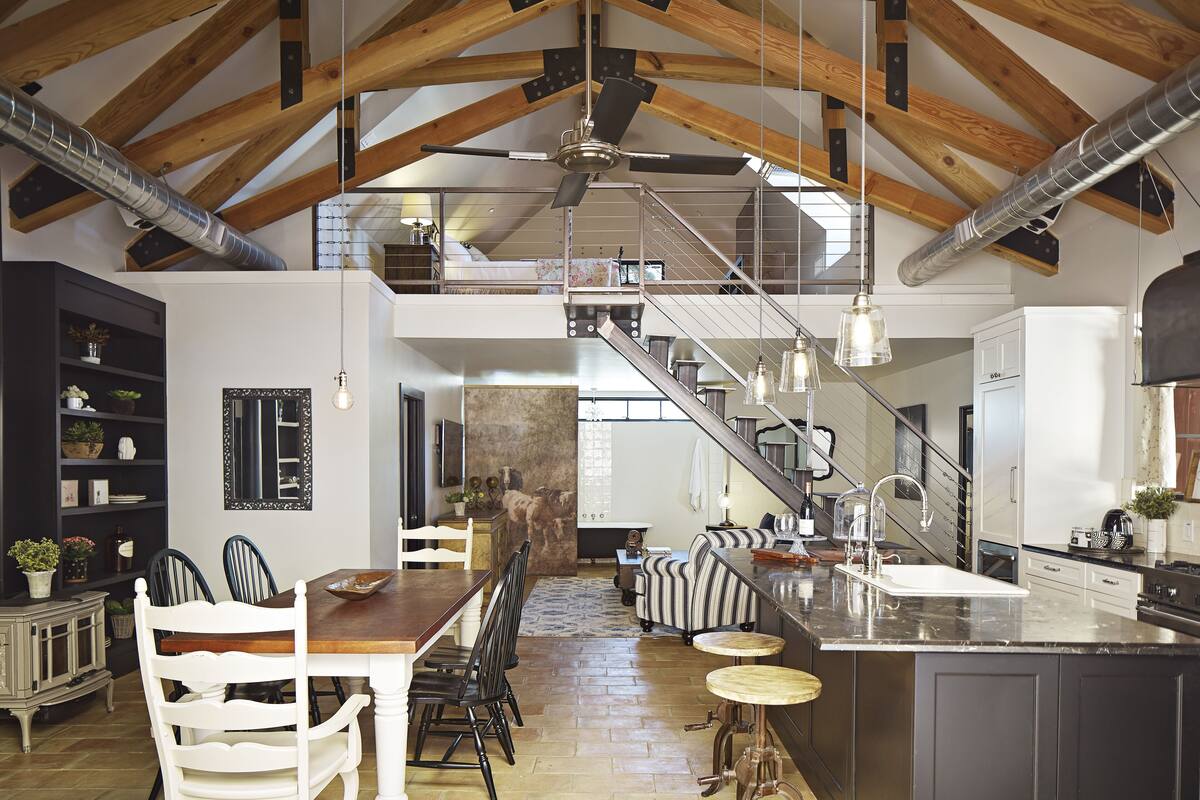 A spacious kitchen with a large island, a dining area with white chairs, and a staircase leading to an upper level.