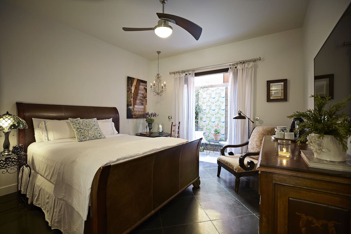 A bedroom with a large bed, a ceiling fan, a nightstand with a lamp, a chair, and a dresser with a mirror.