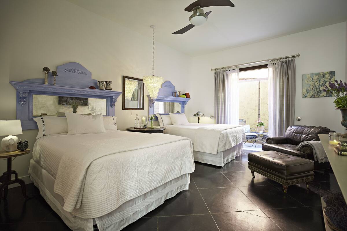 A hotel room with two beds, a sitting area with a leather sofa, a chandelier, and a ceiling fan.