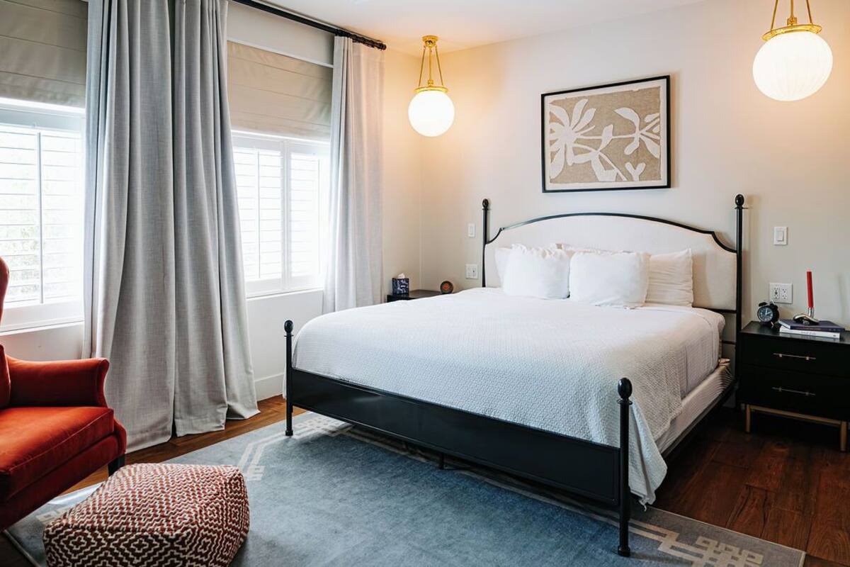 A bedroom with a bed, a nightstand, a chair, and a window with curtains.