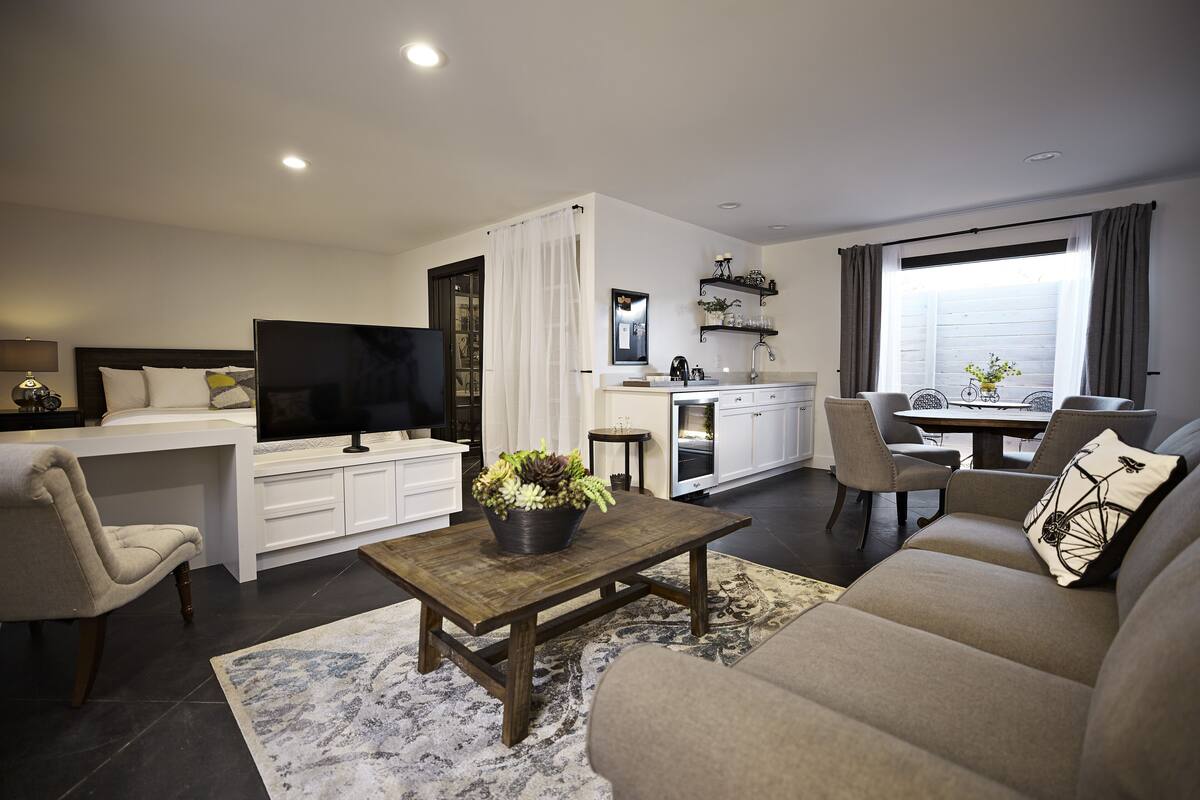 A modern living room with a sofa, a coffee table with a plant, a TV, and a kitchen area with a dining table.