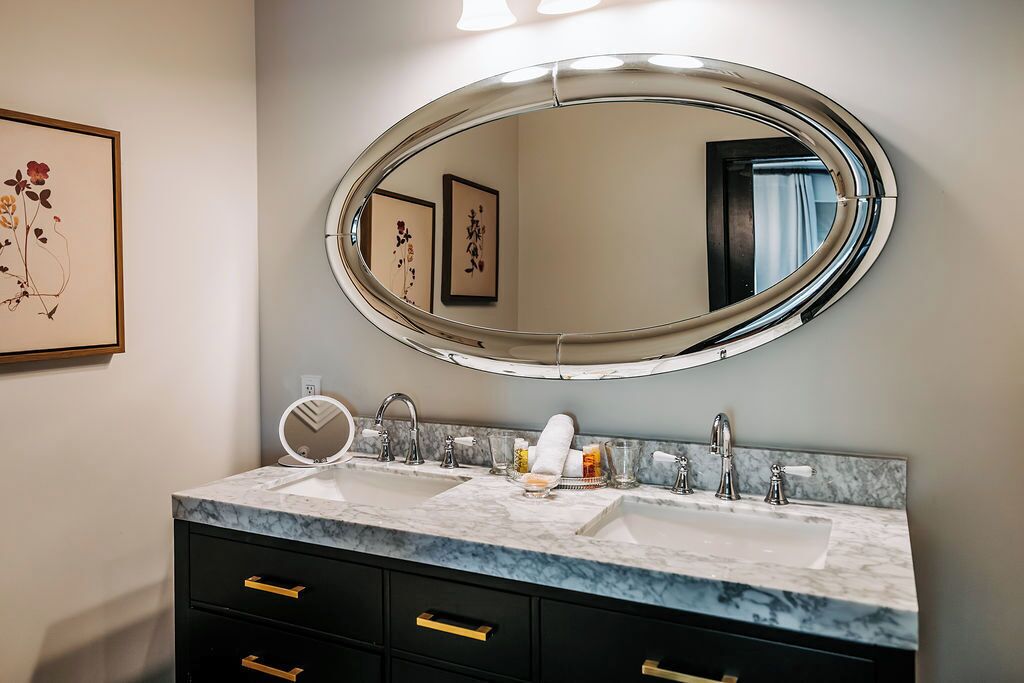 A bathroom with two sinks, a large oval mirror, and a marble countertop.