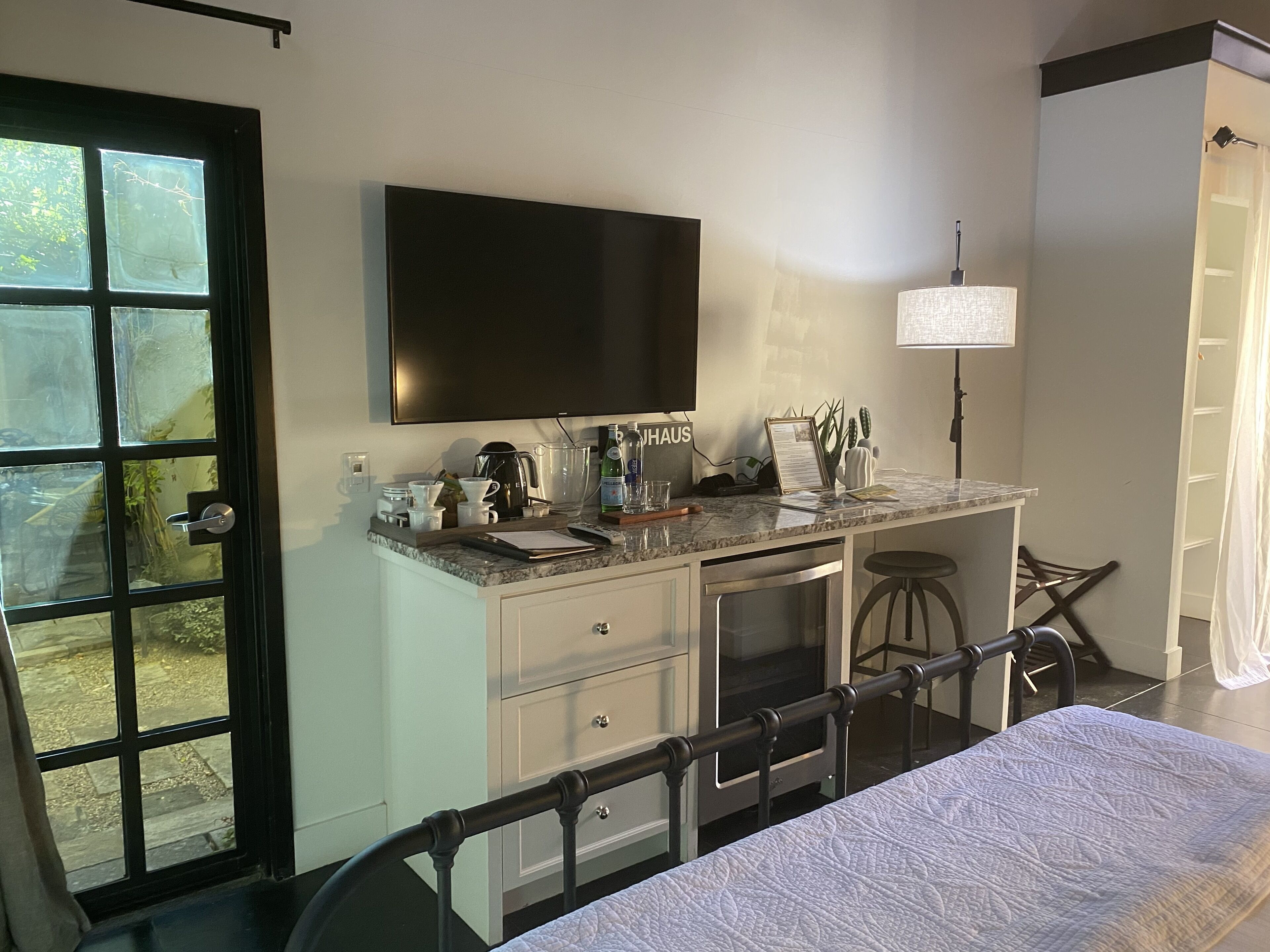 A bedroom with a bed, a desk with a computer, a TV, and a window with a view of the outdoors.