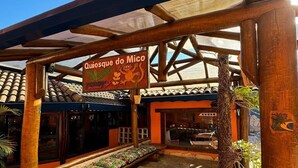 A covered outdoor seating area with a sign reading "Quiosque do Mico" and a palm tree. - Hotel Pousada Tambayba (Sao Sebastiao)