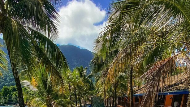 A pool area with lounge chairs and palm trees, surrounded by buildings with balconies. - Hotel Pousada Tambayba (Sao Sebastiao)