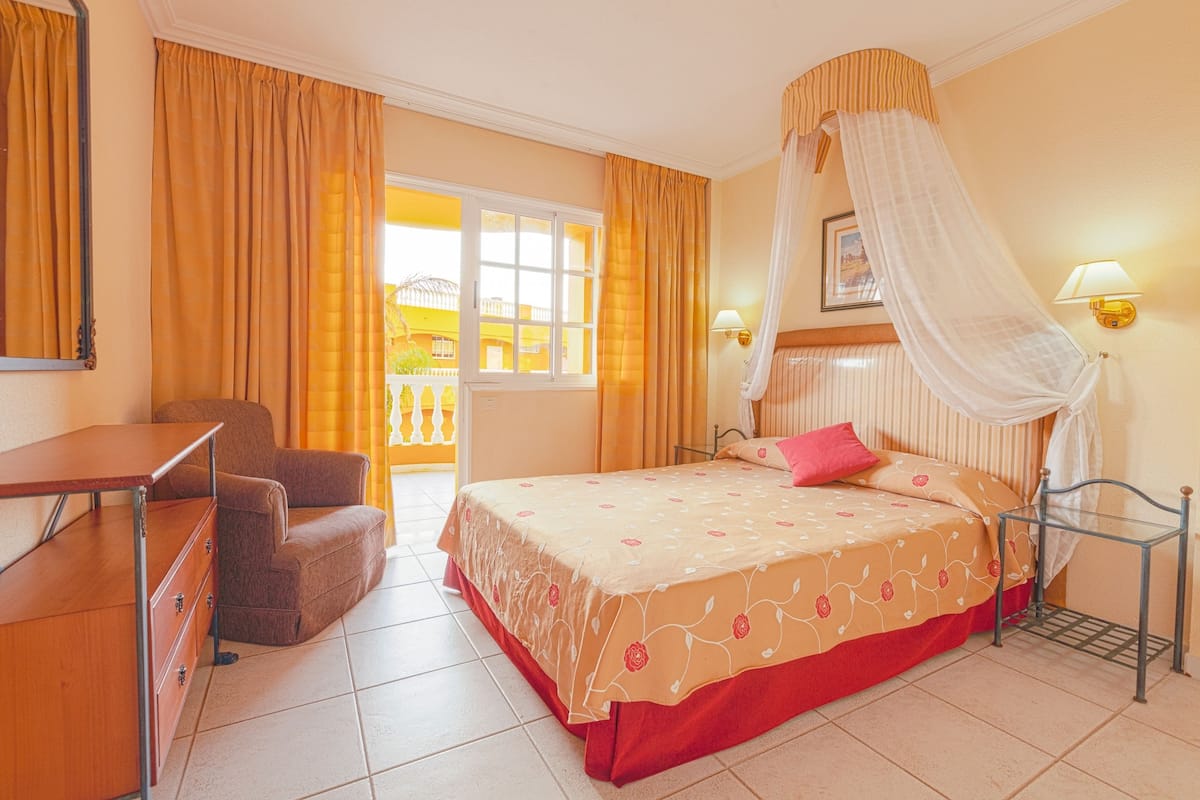 A hotel room with a bed, a desk, a chair, and a window with curtains.