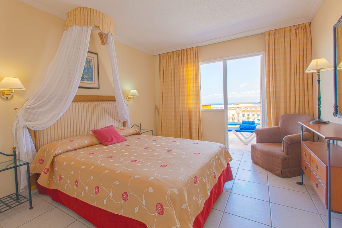A hotel room with a bed, a chair, a desk, and a balcony with a view.