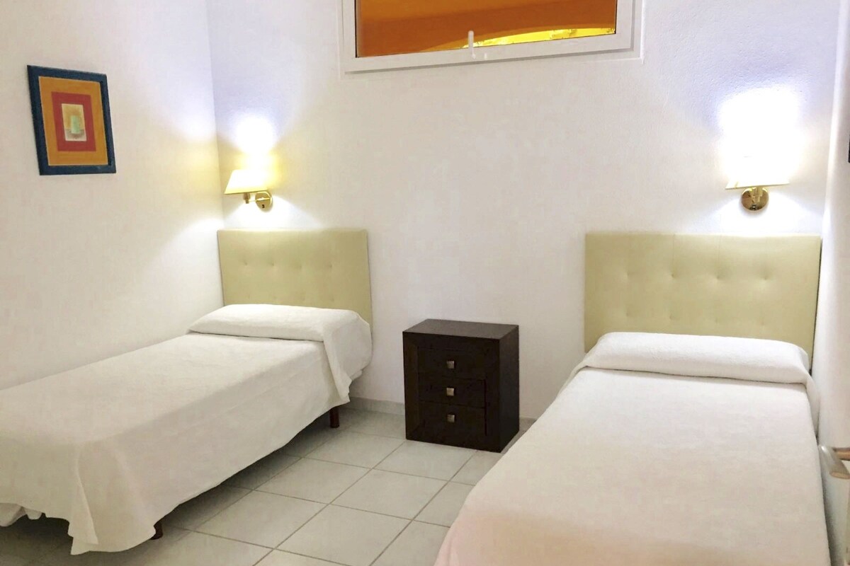 Una habitación con dos camas, un mueble pequeño de color oscuro y un cuadro colgado en la pared.