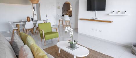 Una sala de estar moderna con sofá, sillones, una mesa de centro y un televisor montado en la pared.