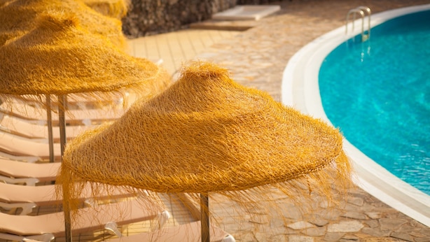 Zona de piscina con sillas de descanso y sombrillas de paja.