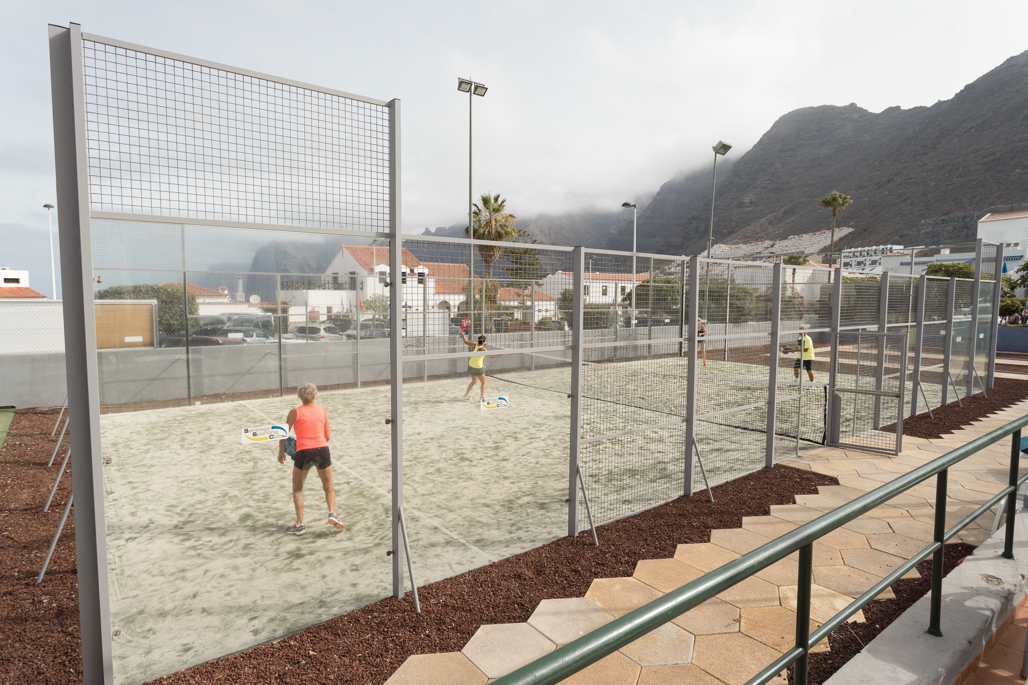 A beach volleyball court with a net, surrounded by a fence and a metal railing.