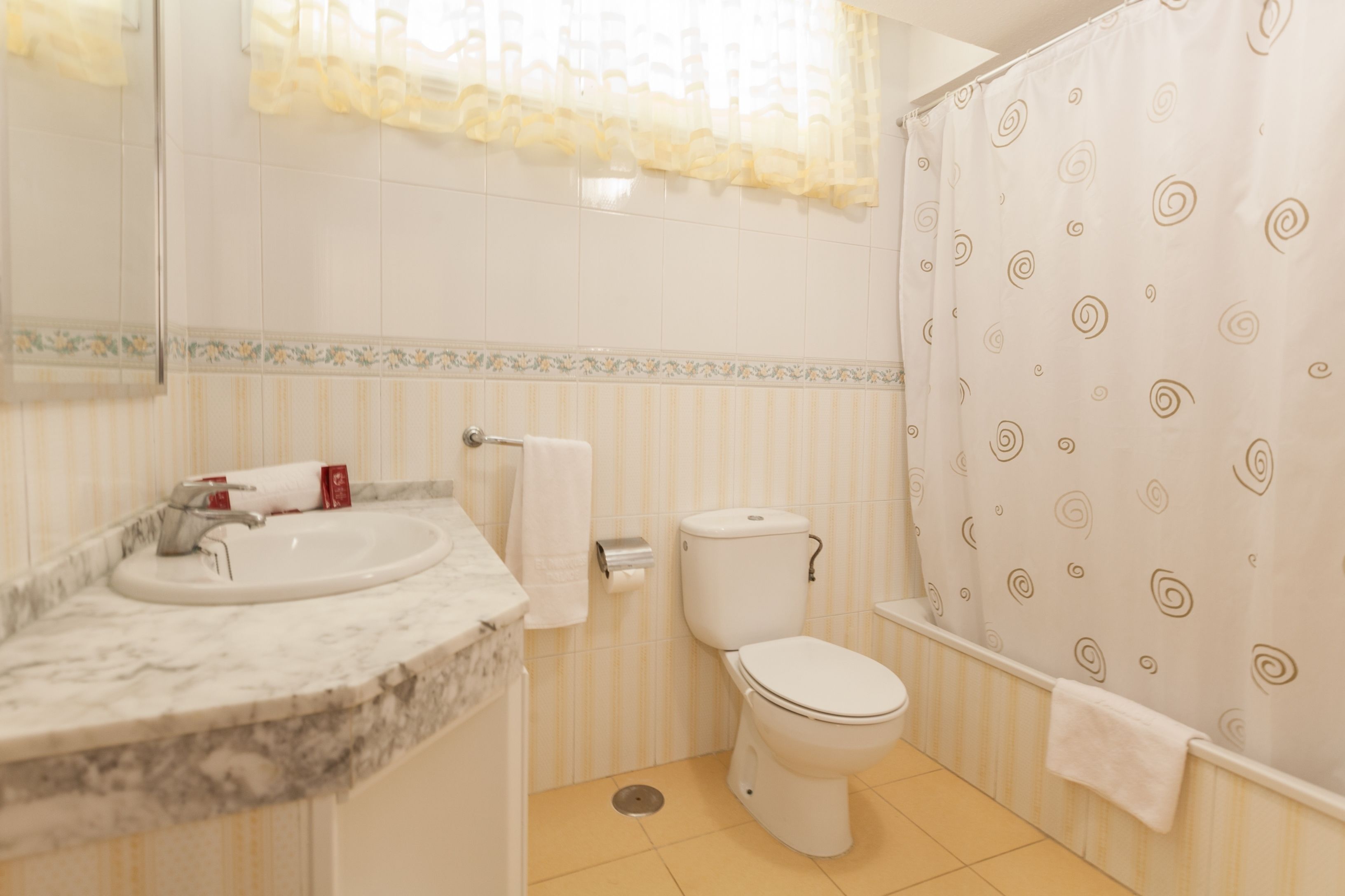 Un baño con lavamanos, inodoro y cortina de ducha de diseño en espiral de mármol.