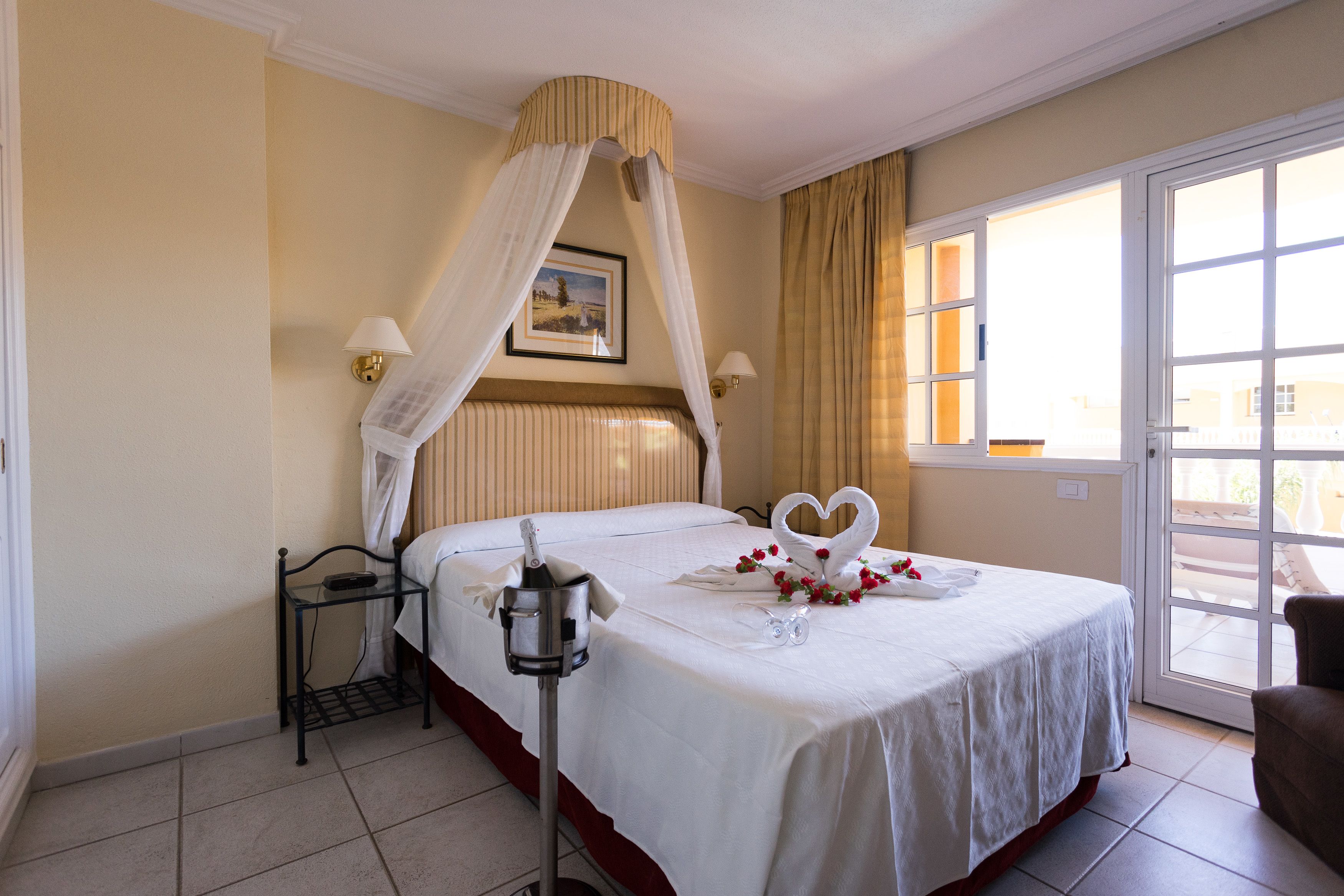 Une chambre d’hôtel avec un lit, une table de chevet, une lampe, une fenêtre avec des rideaux et une vue sur l’extérieur.