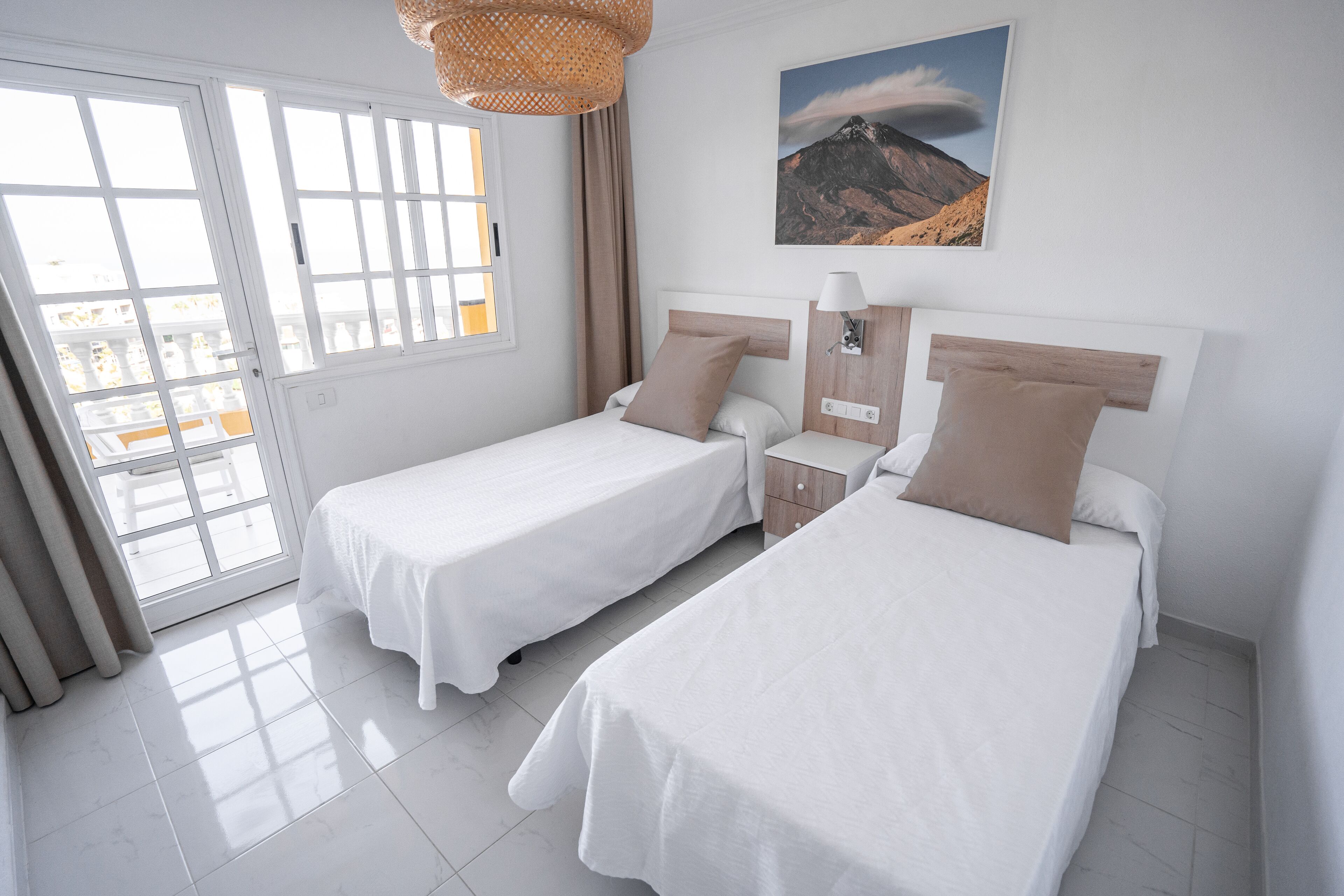 A hotel room with two beds, a window with a view of the mountains, and a door leading to a balcony.