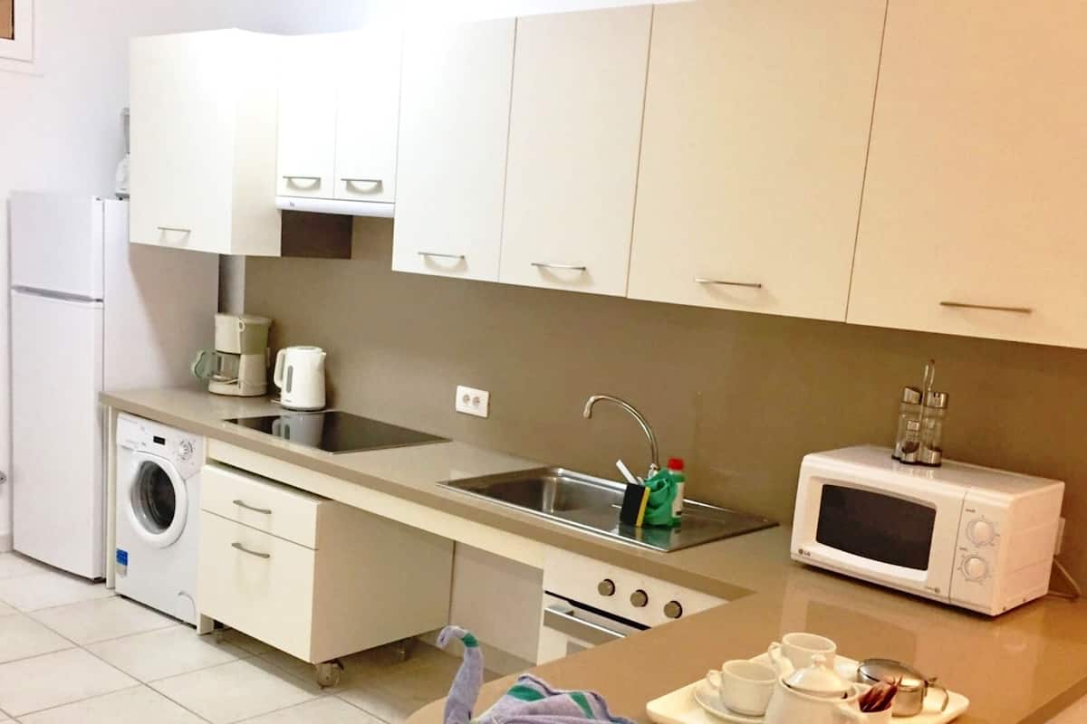 A compact kitchen with a washing machine, microwave, sink, and a small dining area with a tray of cups and utensils.