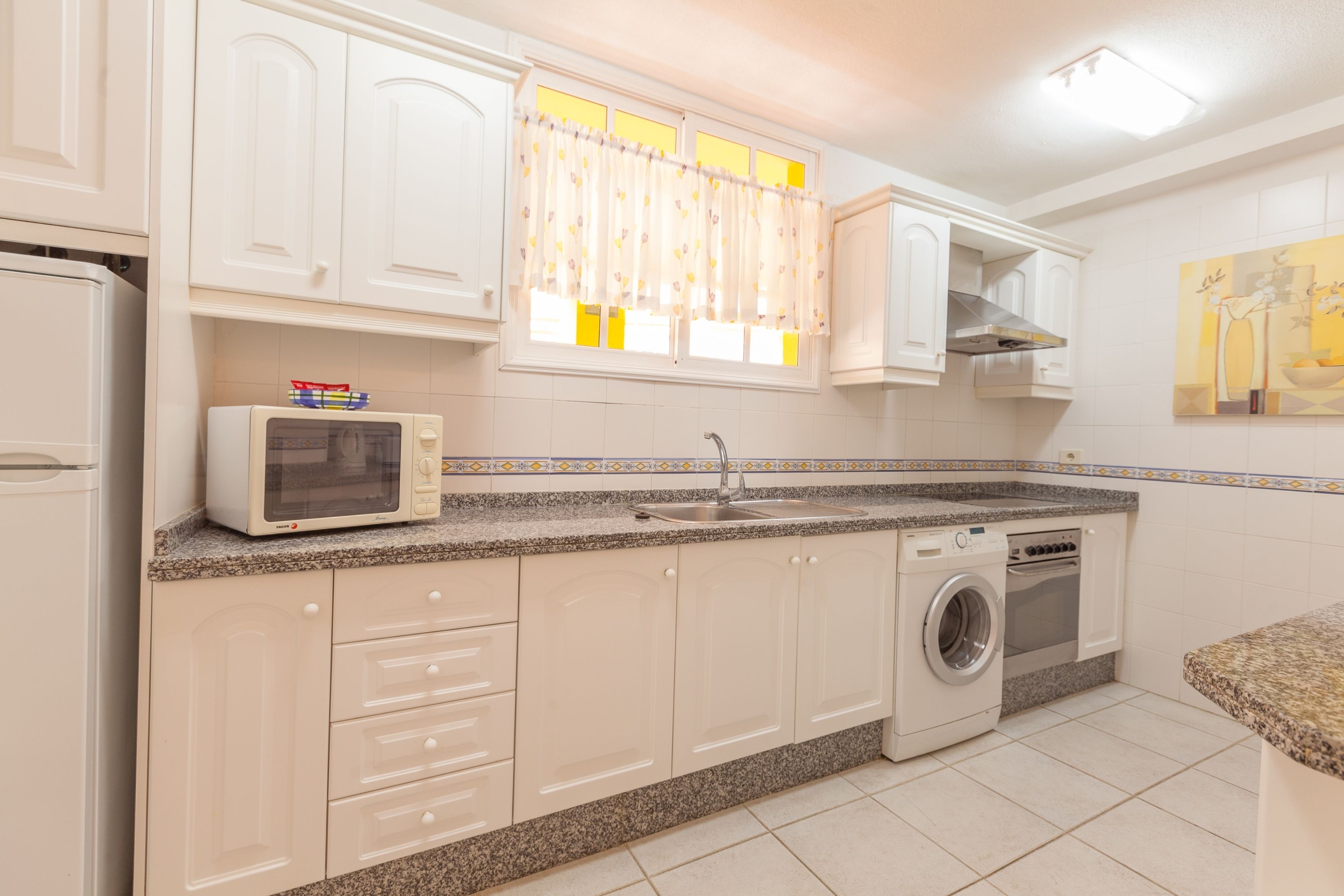 Une cuisine avec des meubles blancs, un four à micro-ondes, un lave-linge et un évier.